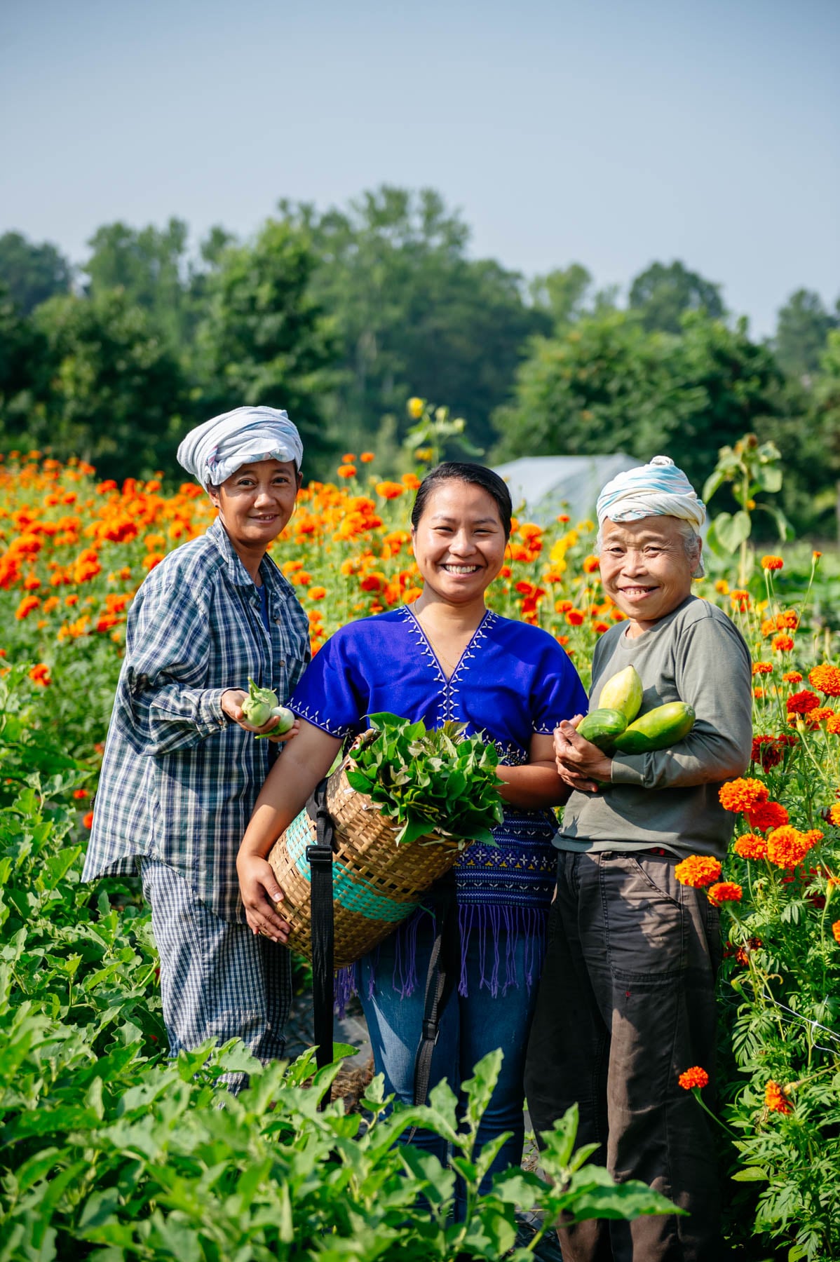 Paw Moo, Ree Ree Wei and Ha Na stand in one of the vegetable patches by the marigolds.