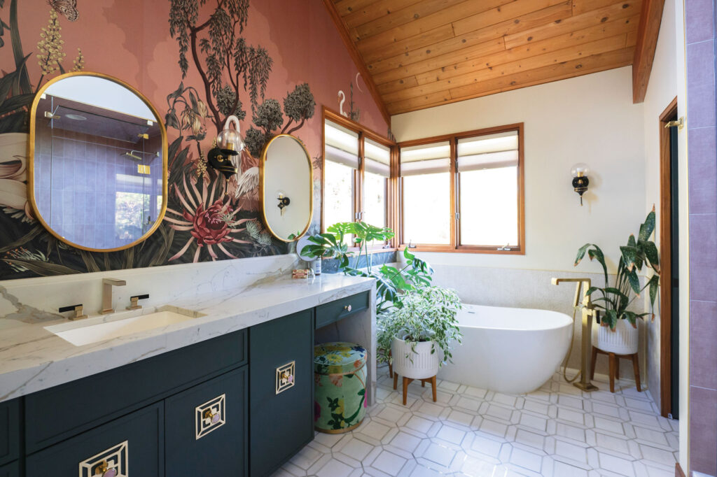 Interior designer Ana Tavares’s half-bath is patterned with botanical wallpaper and includes a tub surrounded by plants.