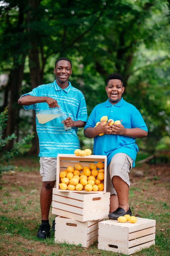 Amir Lyons and Corey Clay Jr. of King’s Lemonade standing with crates of lemons and a pitcher of lemonade.