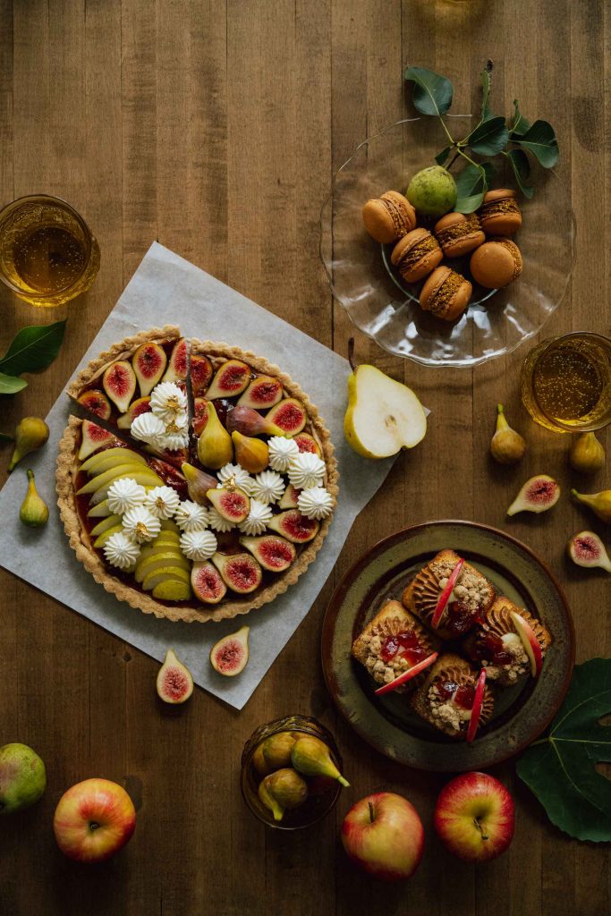Fall desserts and pastries arranged with figs, pears and apples on a wooden table.