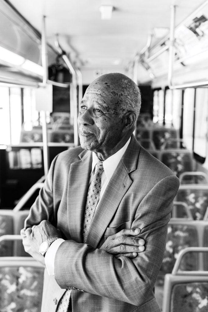 Mayor Howard Lee in a suit standing inside a bus with his arms crossed.