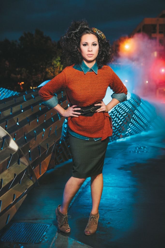 Model in an orange sweater and skirt posing in front of a metal art installation at night in Chapel Hill.