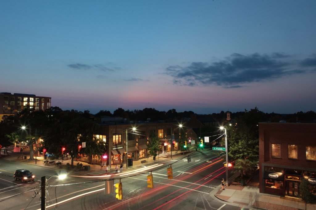 Franklin Street in Chapel Hill at dusk with storefronts lit and light trails from passing cars.