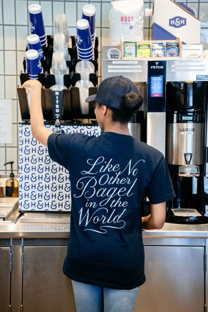 H&H Bagels employee makes fresh coffee wearing a T-shirt referencing the brand's NYC-style water bagels.