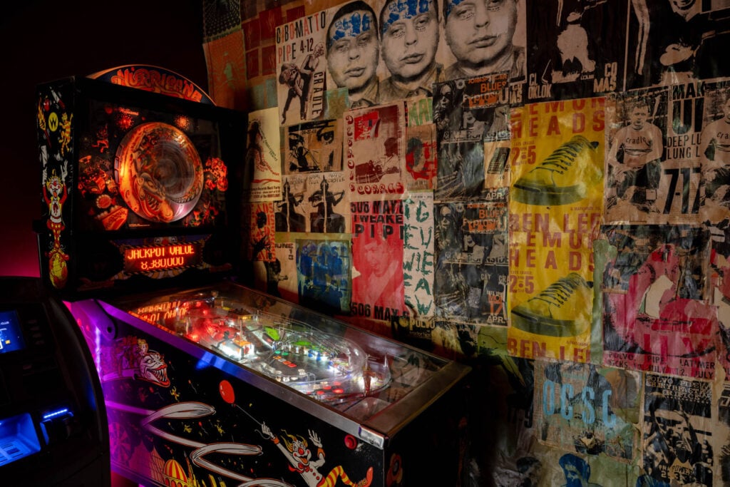 The Pinball machine sits against a wall with posters inside OCSC.